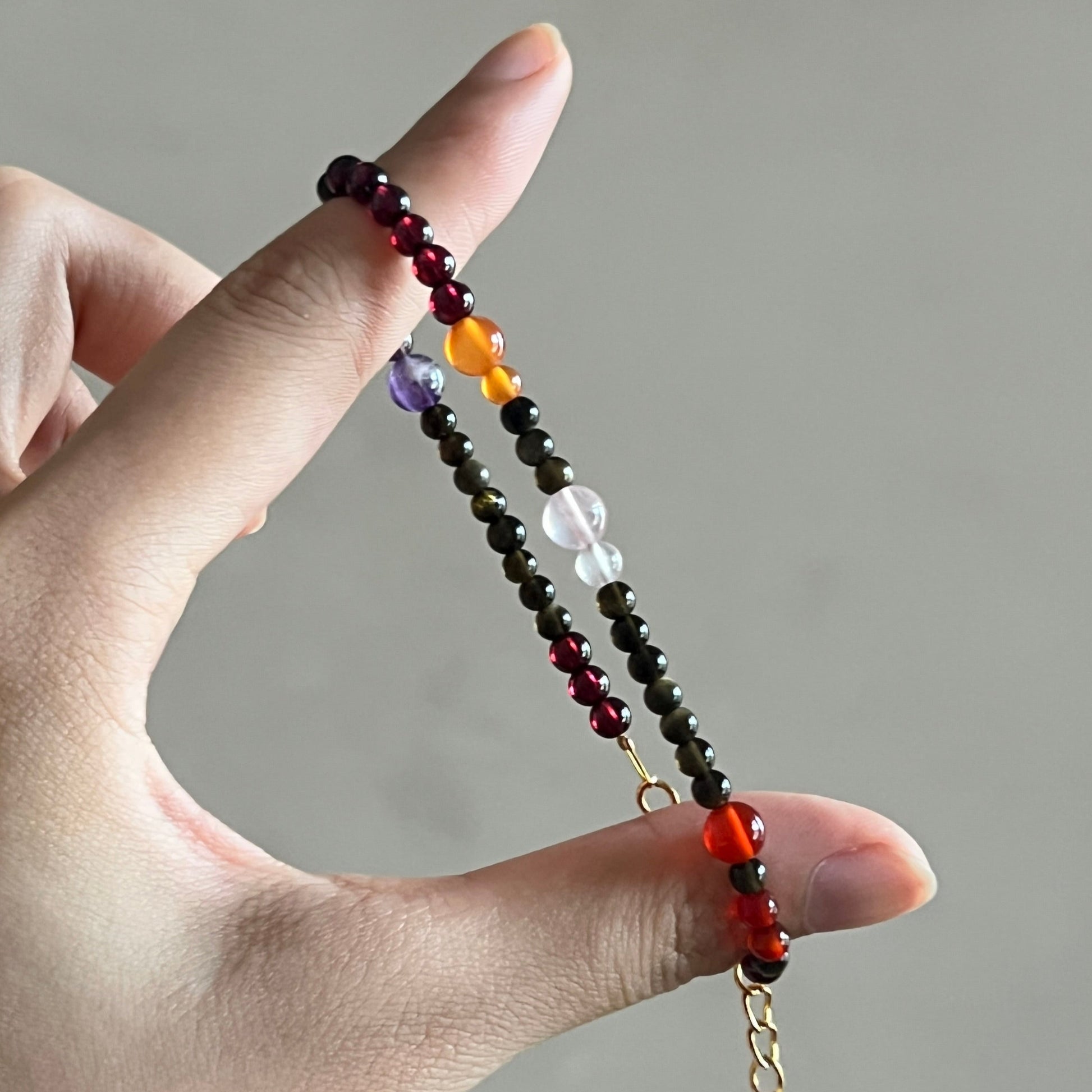 Hand holding a beaded bracelet with a chain against a neutral background