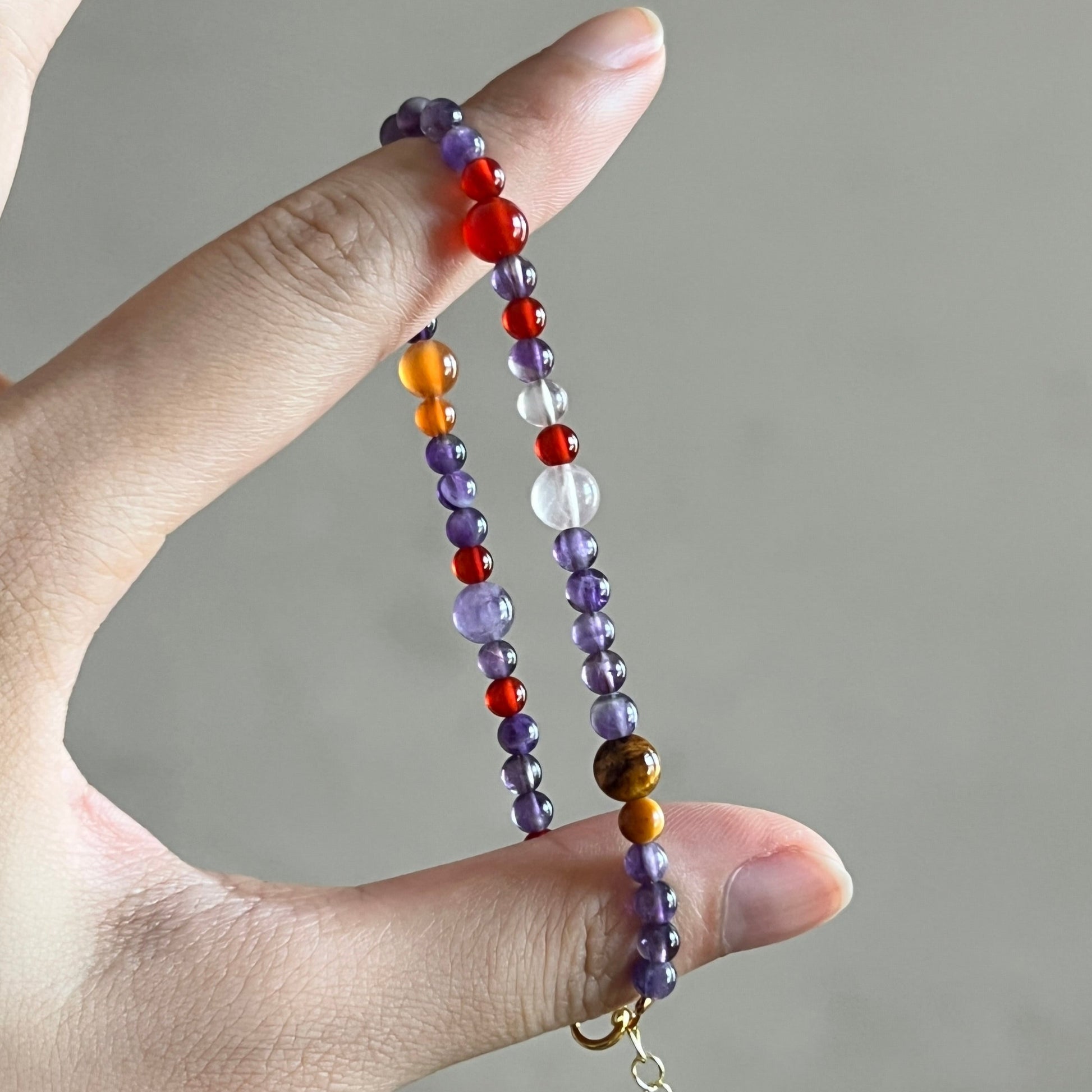 Hand holding a colorful beaded bracelet against a neutral background