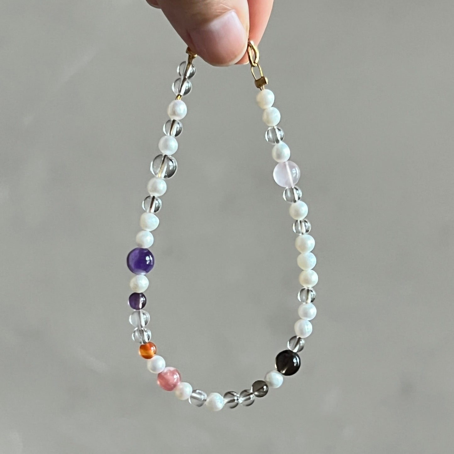 Hand holding a beaded bracelet with multicolored beads against a neutral background