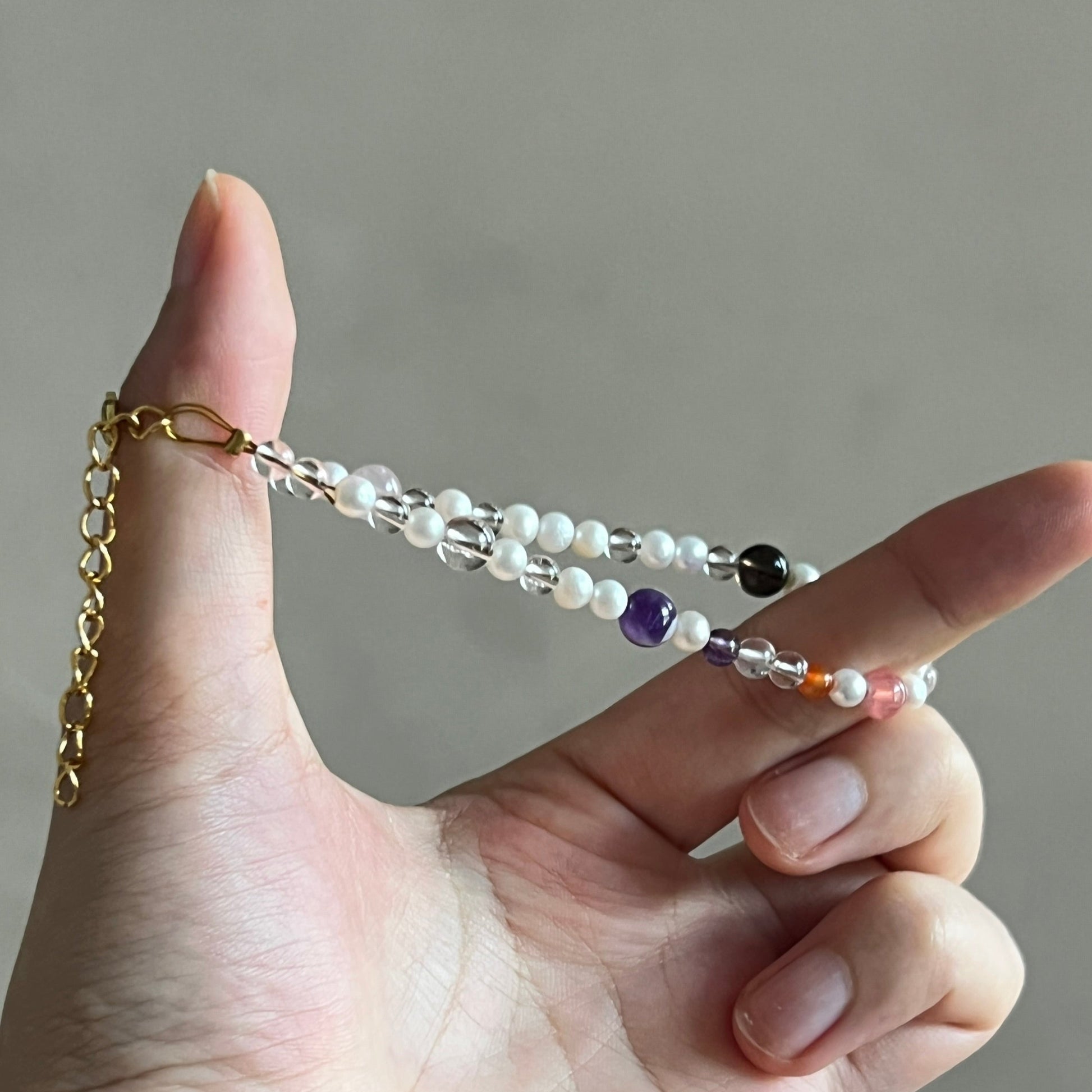 Hand holding a beaded chain with pearls and colored beads against a neutral background
