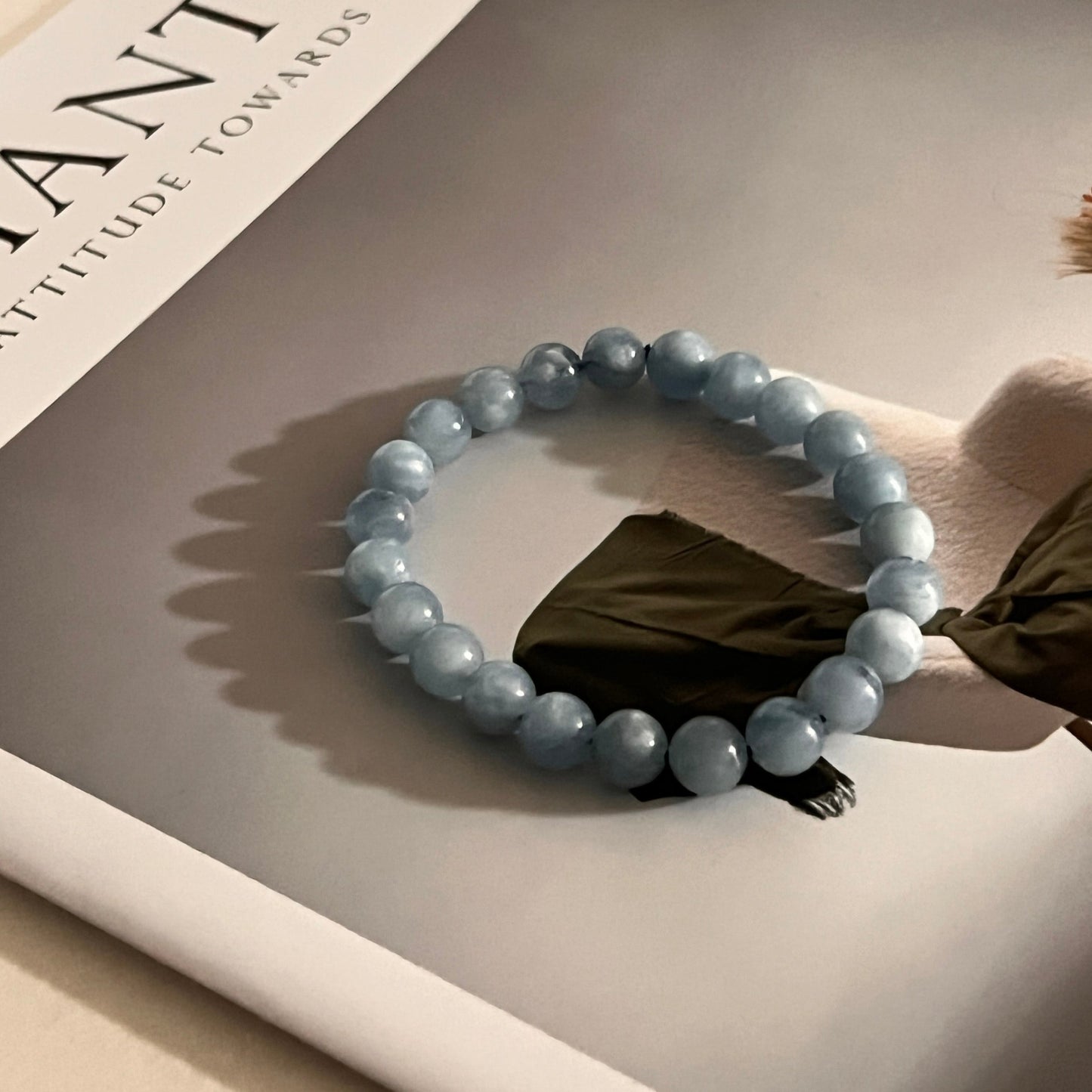 Beaded aquamarine bracelet on a reflective surface with a book titled 'FANTIC' in the background