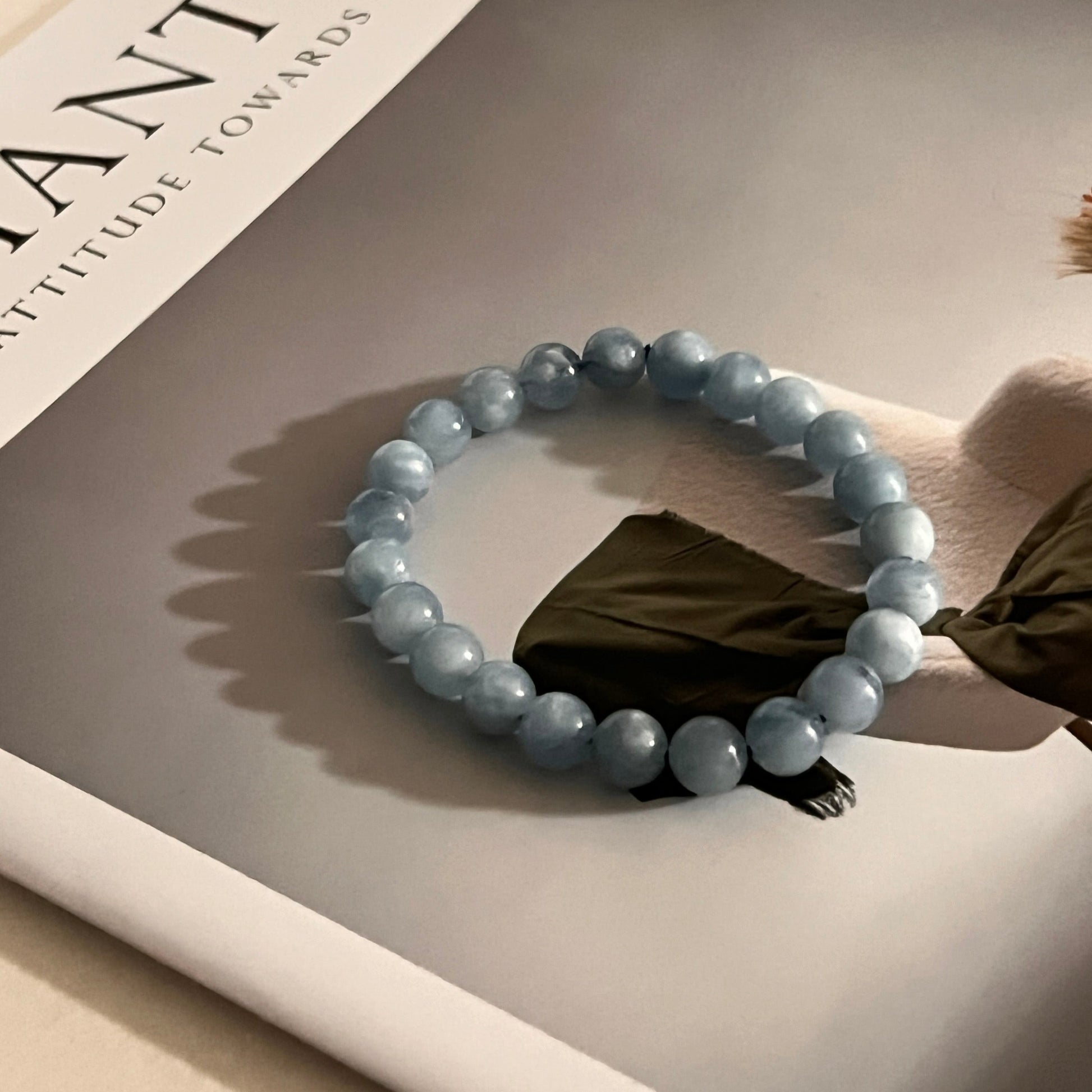 Beaded aquamarine bracelet on a reflective surface with a book titled 'FANTIC' in the background
