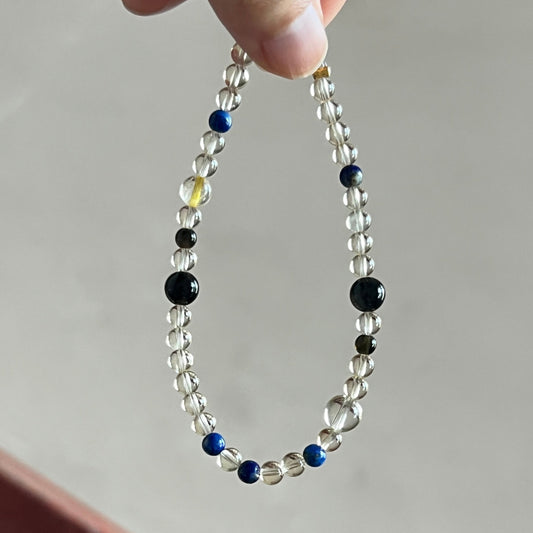 Necklace with clear, black, and blue beads held by a hand against a neutral background