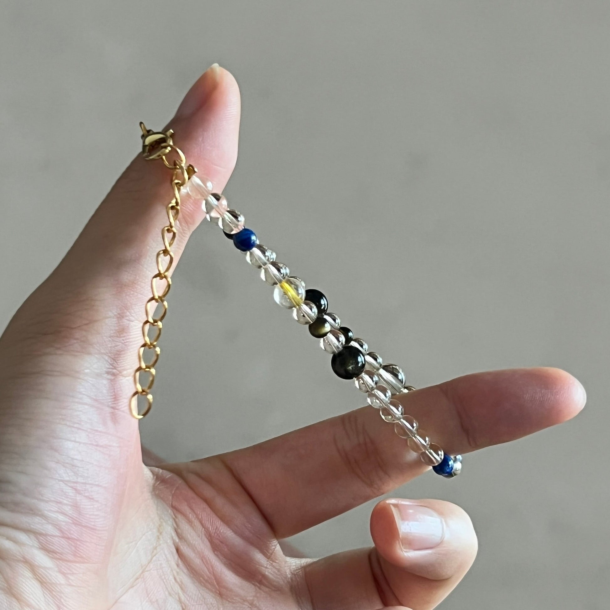 Hand holding a delicate bracelet with small beads against a neutral background