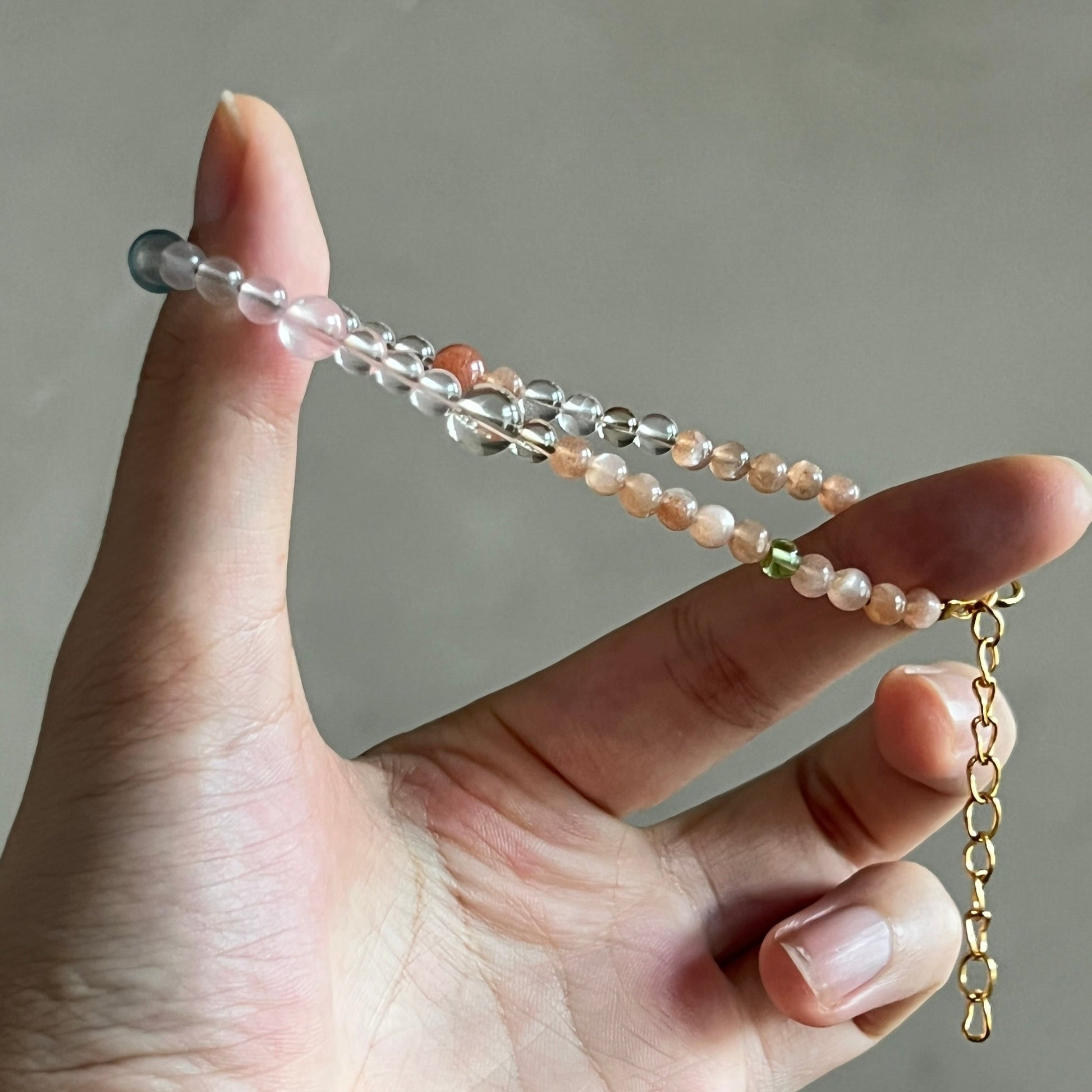 Hand holding a delicate bracelet with beads on a neutral background