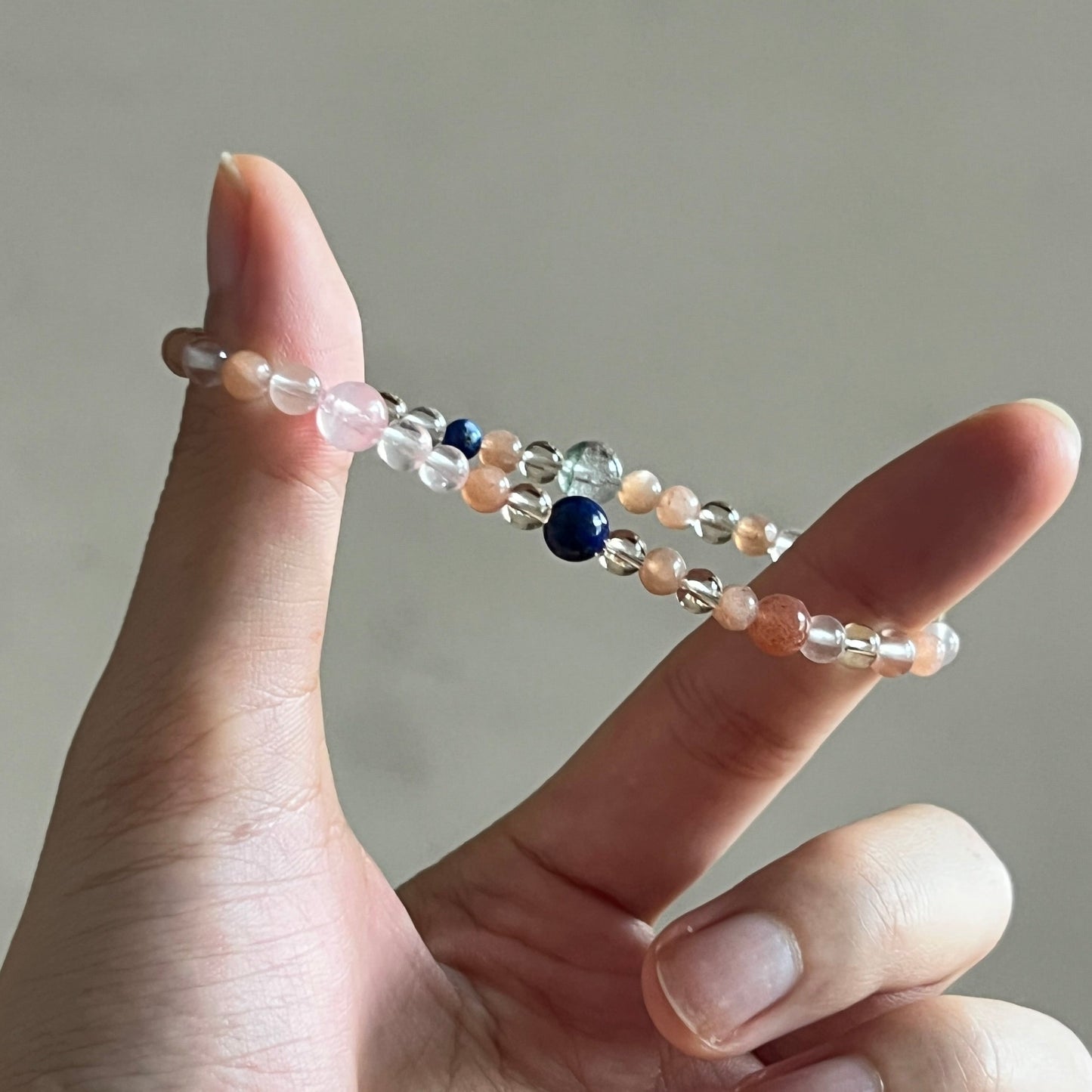 Hand wearing a beaded bracelet on a neutral background