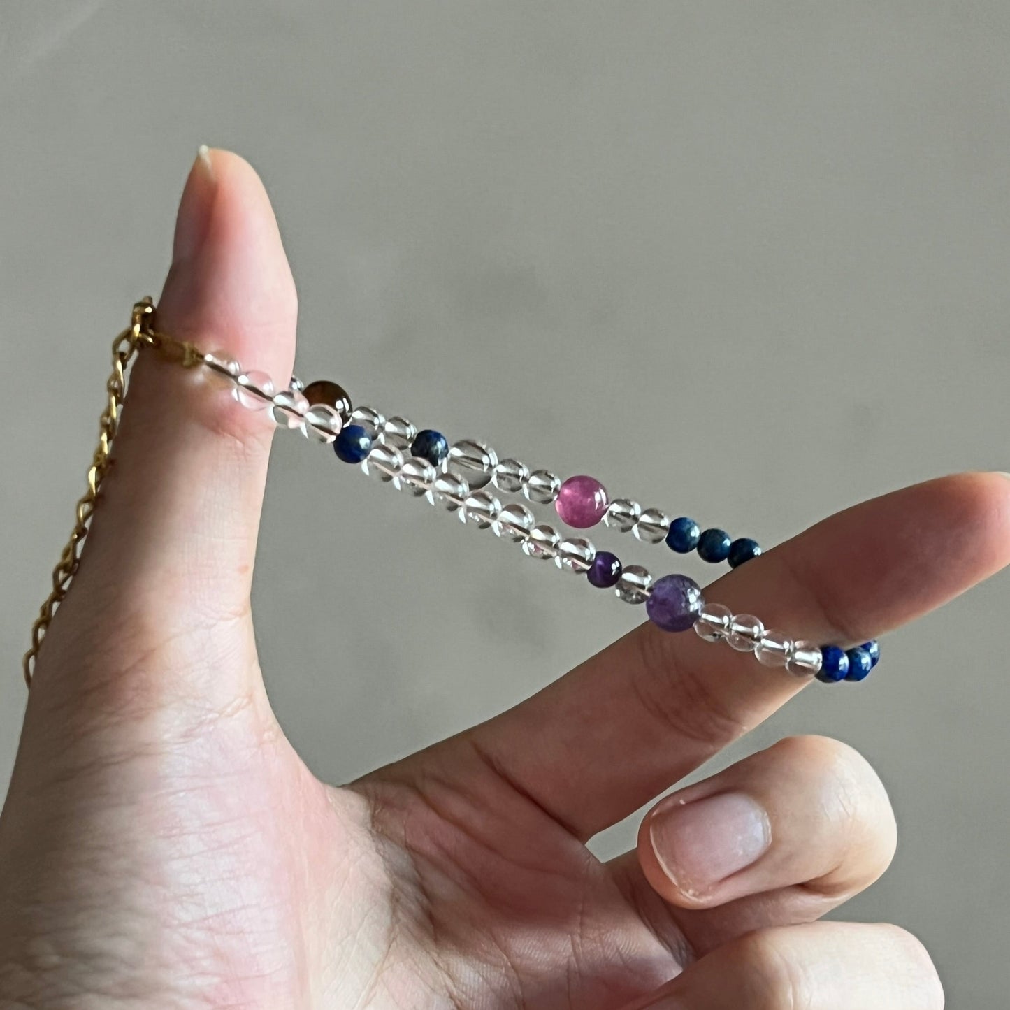 Hand holding a crystal bracelet with colorful beads against a neutral background
