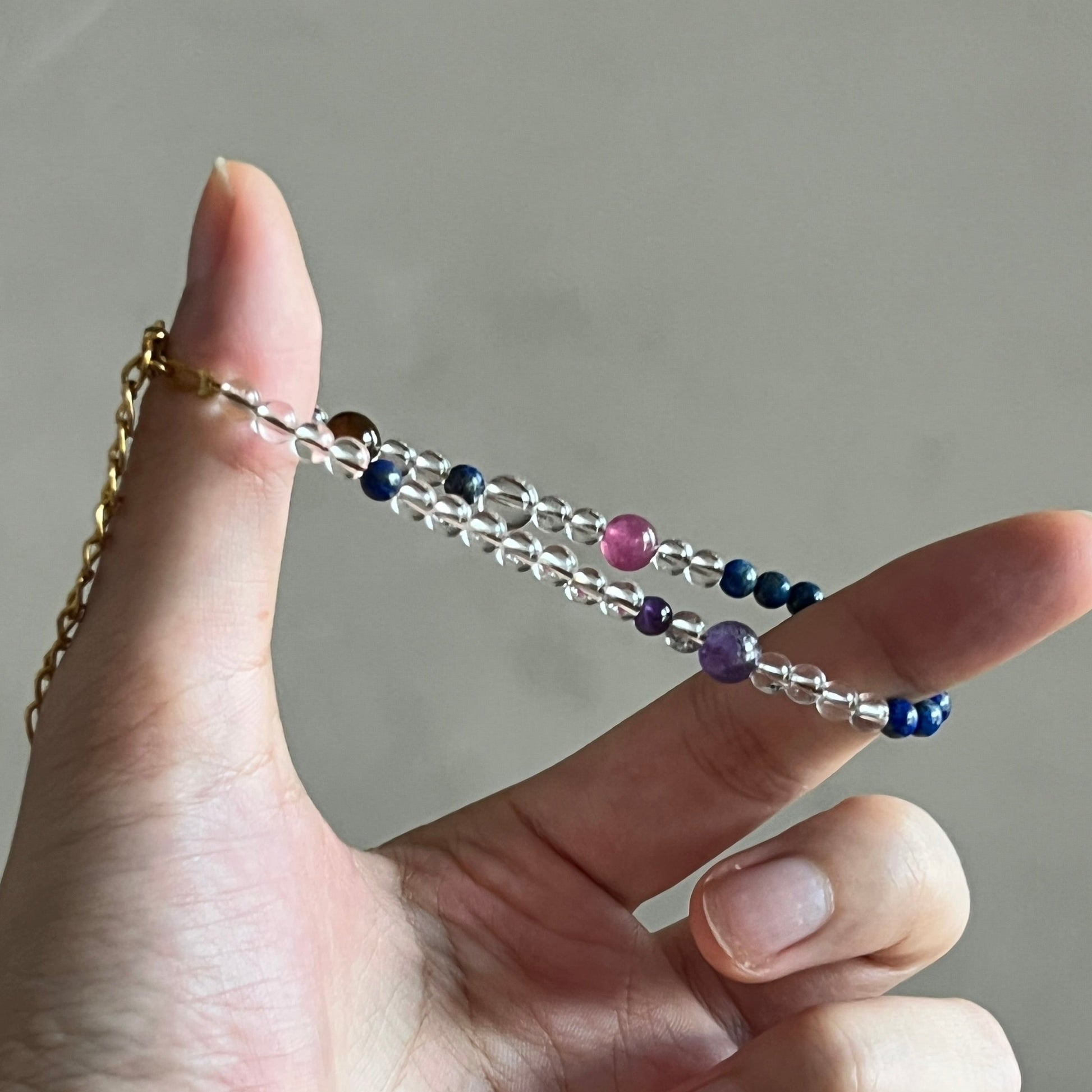 Hand holding a crystal bracelet with colorful beads against a neutral background