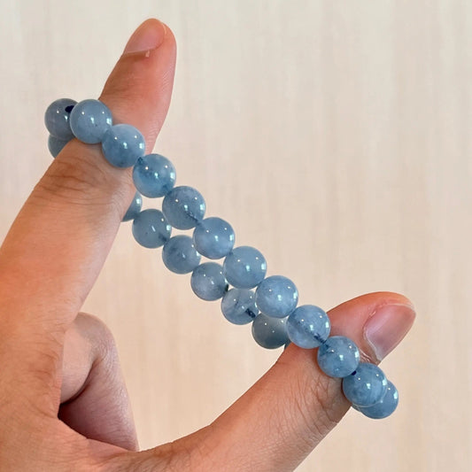 Hand holding a blue beaded aquamarine bracelet against a plain background